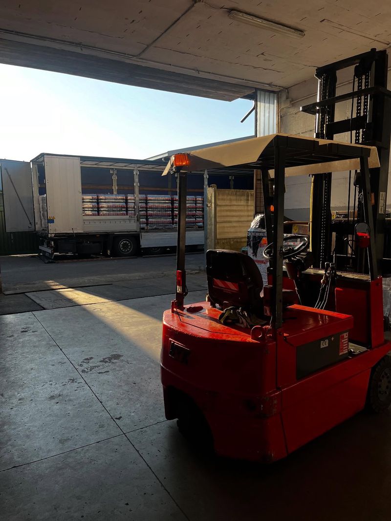 Carrello elevatore nel magazzino di Seregno, con un camion telonato carico di pallet sulla baia di carico